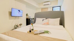A hotel room with a bed, a television mounted on the wall, an air conditioning unit, and a window. - Comfortable And Minimalist Studio At Apartment Meikarta District 1 (Cikarang)