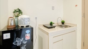 A compact kitchen with a refrigerator, a kettle, a rice cooker, a sink, and a small potted plant. - Comfortable And Minimalist Studio At Apartment Meikarta District 1 (Cikarang)