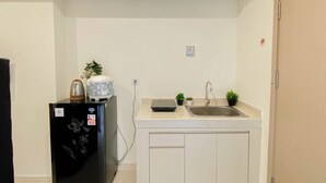 A compact kitchen with a refrigerator, a kettle, a rice cooker, a sink, and two small potted plants. - Comfortable And Minimalist Studio At Apartment Meikarta District 1 (Cikarang)