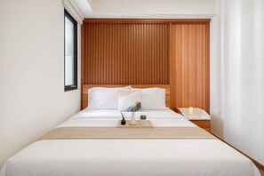 Hotellihuone, jossa on puinen sängynpääty, valkoisilla lakanoiden koristeltu sänky, yöpöytä lampun kanssa ja ikkuna.