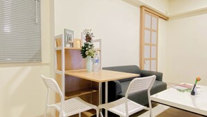 A small, neatly arranged room with a wooden table, two white chairs, a grey sofa, a small shelf with decorative items, and a door. - Good And Minimalist 2Br At Apartment Meikarta District 1 (Cikarang)