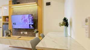 A hotel reception area with a flat-screen TV mounted on a wall, a reception desk, a chair, a vase with flowers, and a thermostat on the wall.