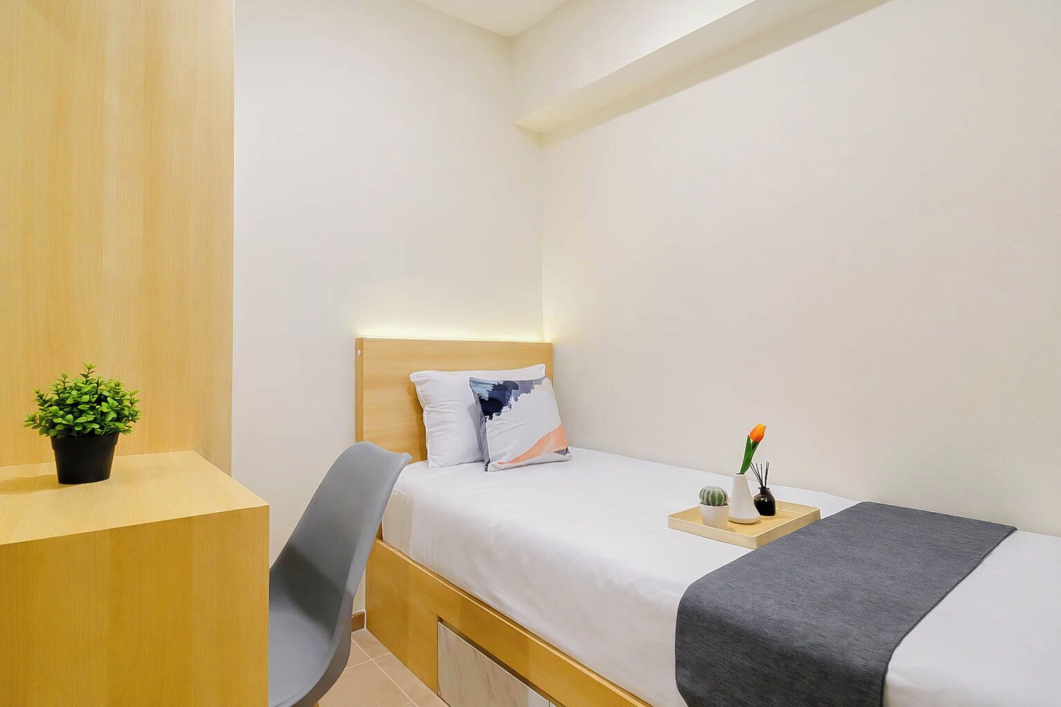 Ein kleines, aufgeräumtes Schlafzimmer mit Bett, Nachttisch, Stuhl und einem Topf mit Pflanze.