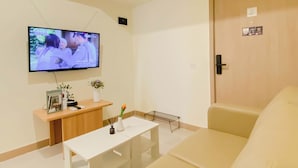 A living room with a television, a sofa, a coffee table, and a door. - Serene Beige 2Br Space At Apartment Meikarta District 1 (Cikarang)