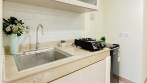 A kitchen with a sink, a small potted plant, a coffee machine, and a trash bin. - Serene Beige 2Br Space At Apartment Meikarta District 1 (Cikarang)