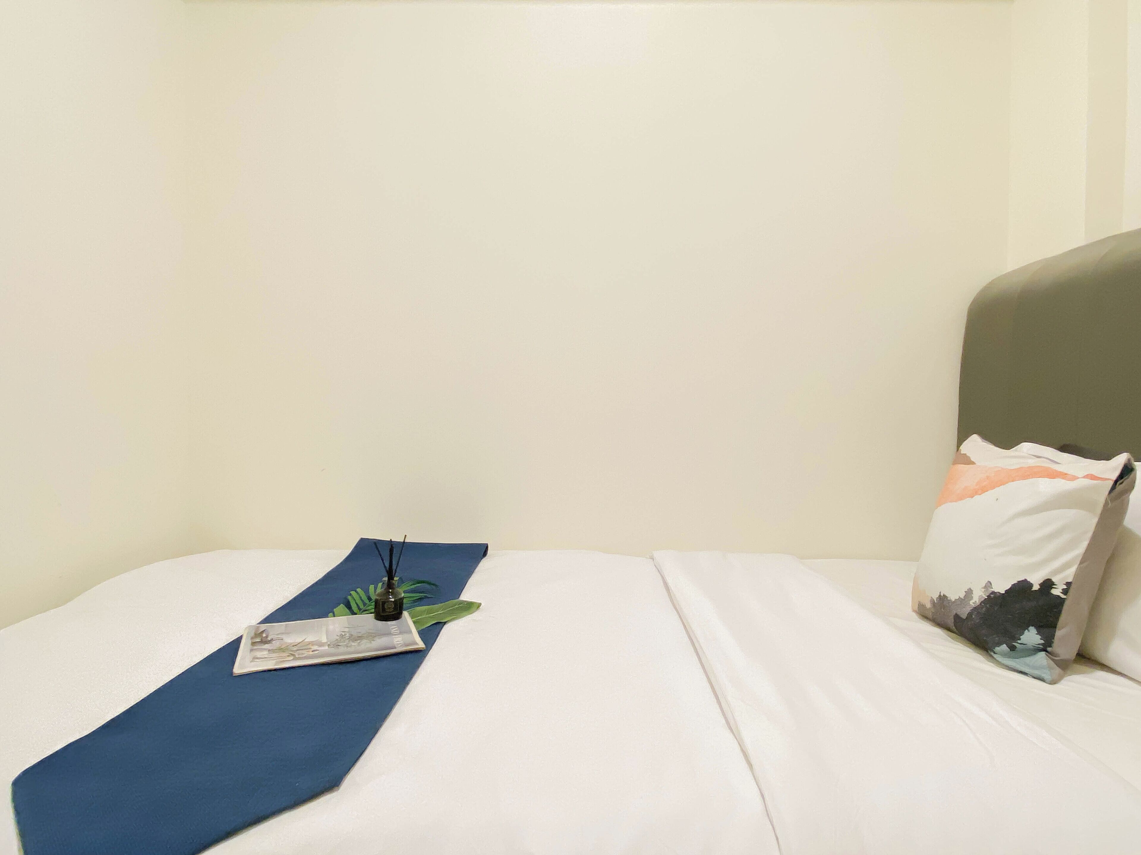 A neatly made bed with a blue bed runner, a pillow with a mountain design, and a small plant on the bed.