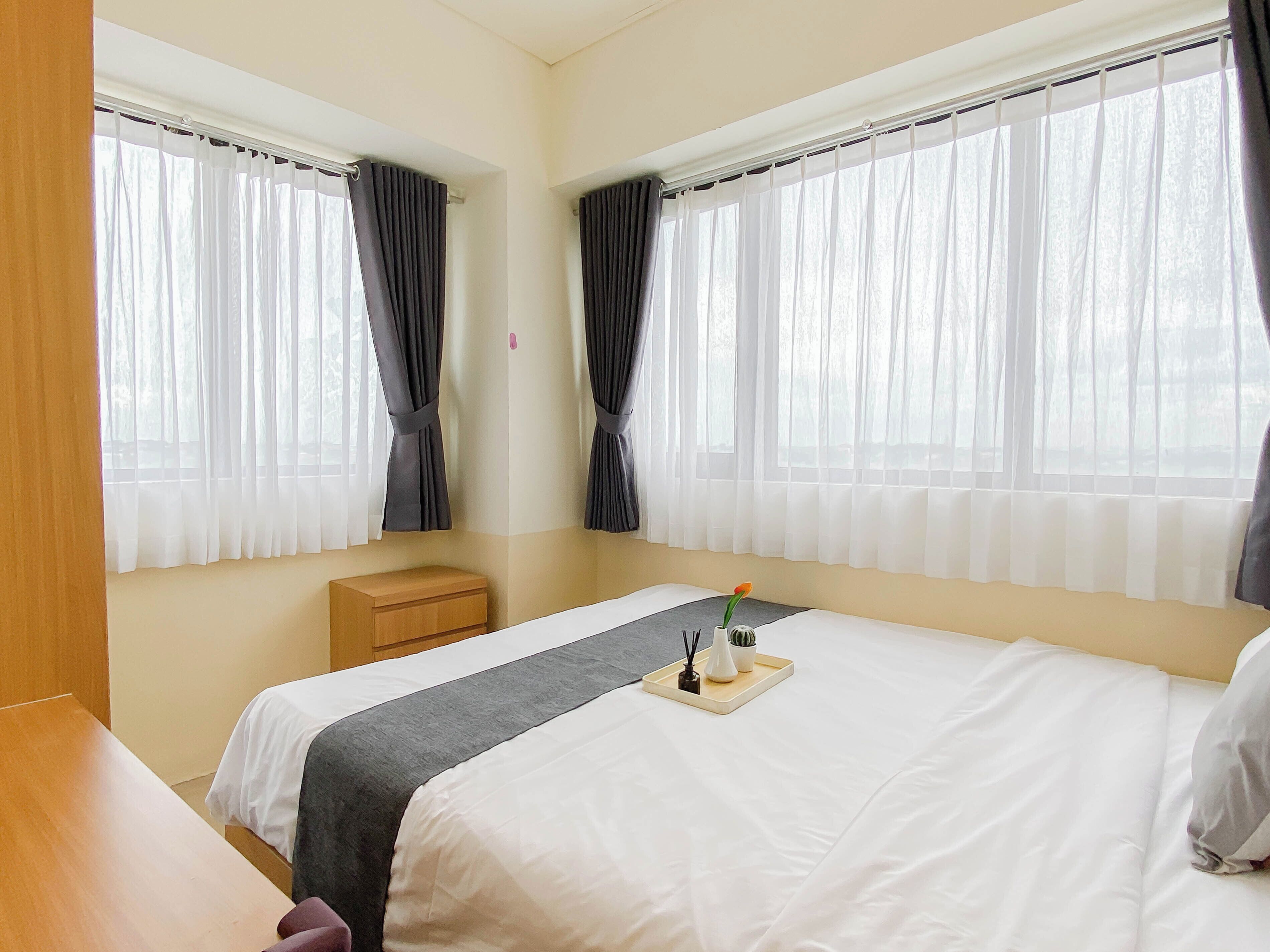 A hotel room with two beds, a bedside table, a small wooden nightstand, and a window with curtains.