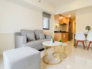 Ein modernes Wohnzimmer mit grauem Sofa, rundem Couchtisch mit goldfarbener Rahmung und Küchenzeile mit Holzschränken und weißen Geräten.