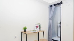 A small room with a table, two stools, a potted plant, and a magazine. - Comfy And Nice Studio Space At Apartment Meikarta District 1 (Cikarang)