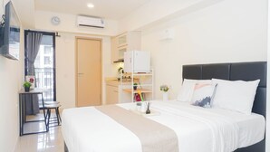 A hotel room with a bed, a desk with a chair, a wardrobe, and a small table with a plant. - Comfy And Nice Studio Space At Apartment Meikarta District 1 (Cikarang)