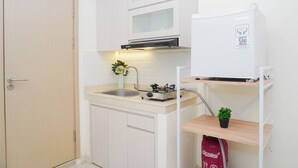A compact kitchen with a gas stove, a sink, and a white refrigerator. - Comfy And Nice Studio Space At Apartment Meikarta District 1 (Cikarang)