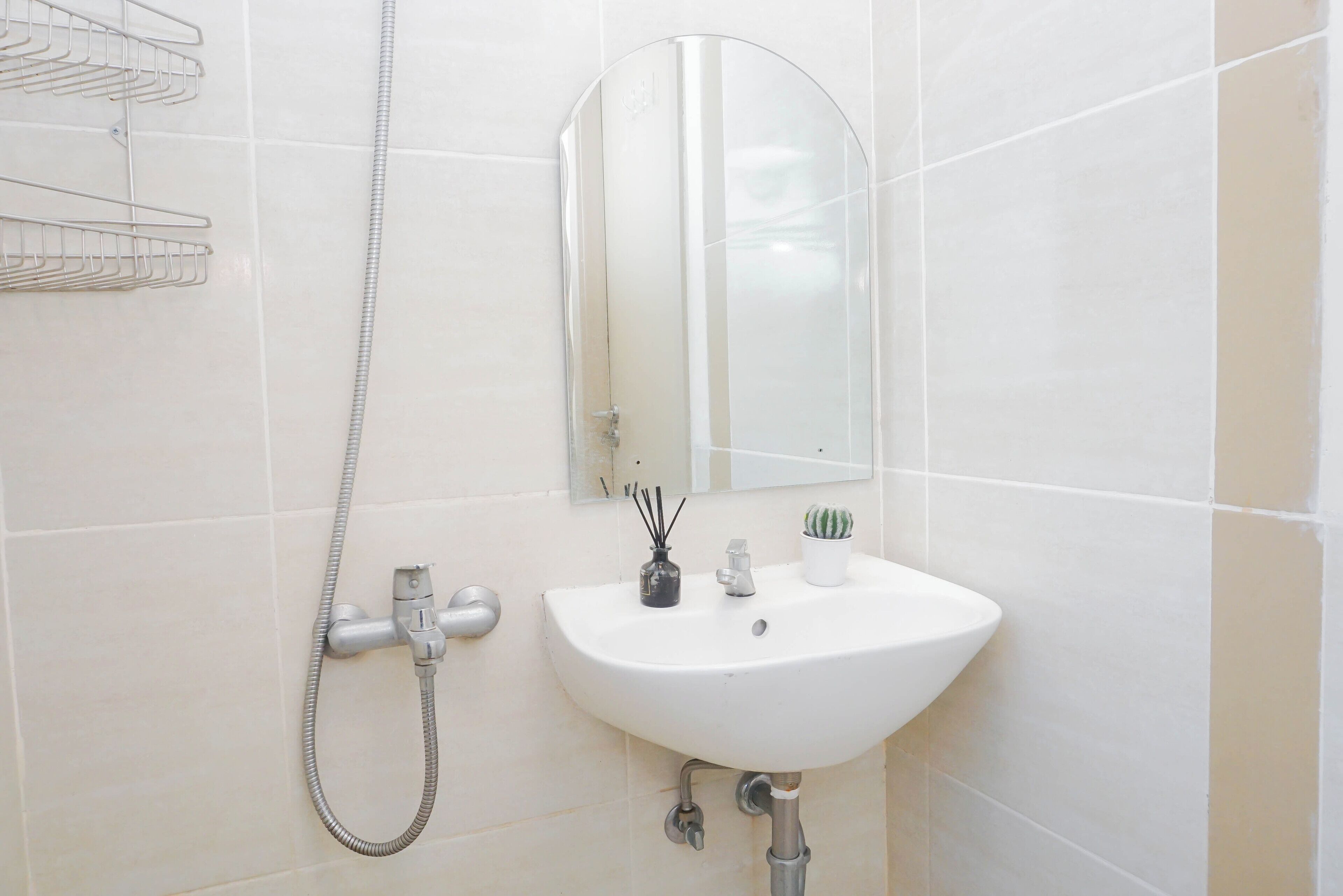 Un baño con lavamanos blanco, un espejo, ducha y un perchero para toallas.