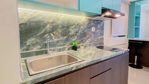 Una cocina con salpicadero de mármol, lavamanos de acero inoxidable, armarios color turquesa e iluminación debajo de los armarios.