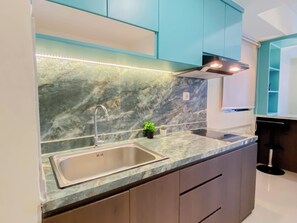 A kitchen with a marble backsplash, stainless steel sink, teal cabinets, and under-cabinet lighting. - Comfy And Nice Cyan 2Br At Apartemen Meikarta District 1 (Cikarang)