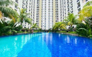 A swimming pool surrounded by tall residential buildings and lush tropical vegetation. - Good Deal Studio At Cinere Resort Apartment (Depok)