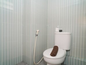 A bathroom with a toilet, a shower hose, and a towel on the seat. - Good Deal Studio At Cinere Resort Apartment (Depok)