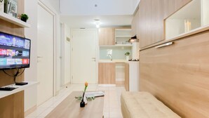 Una sala de estar moderna con un televisor de pantalla plana, una mesa de centro con un jarrón, un sofá beige y una cocina al fondo.