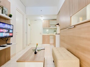 A modern living room with a flat-screen TV, a coffee table with a vase, a beige sofa, and a kitchen area in the background. - Practical 2Br For 4 Pax At Springlake Summarecon Bekasi Apartment (Bekasi)