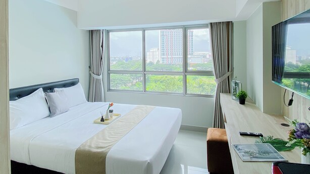 A hotel room with a large bed, a desk, a TV, and a window with a city view. - Best Choice Studio At Springlake Summarecon Bekasi Apartment (Bekasi)