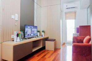 A modern room with a wooden desk, a computer, a red chair, and a window with blinds. - Enjoy Living 2Br At Springlake Summarecon Bekasi Apartment (Bekasi)