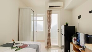 A hotel room with a bed, a TV, a refrigerator, and an air conditioning unit. - Nice And Tidy Studio Room At Apartment Springlake Summarecon Bekasi (Bekasi)