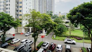 A high-rise residential building with multiple balconies, a parking lot with various cars, and surrounding greenery. - Nice And Tidy Studio Room At Apartment Springlake Summarecon Bekasi (Bekasi)