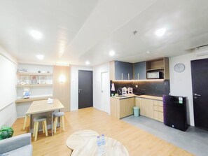 A modern kitchen with a wooden table, chairs, a small island, and a refrigerator. - Cozy 2Br Apartment Grand Asia Afrika (Bandung)