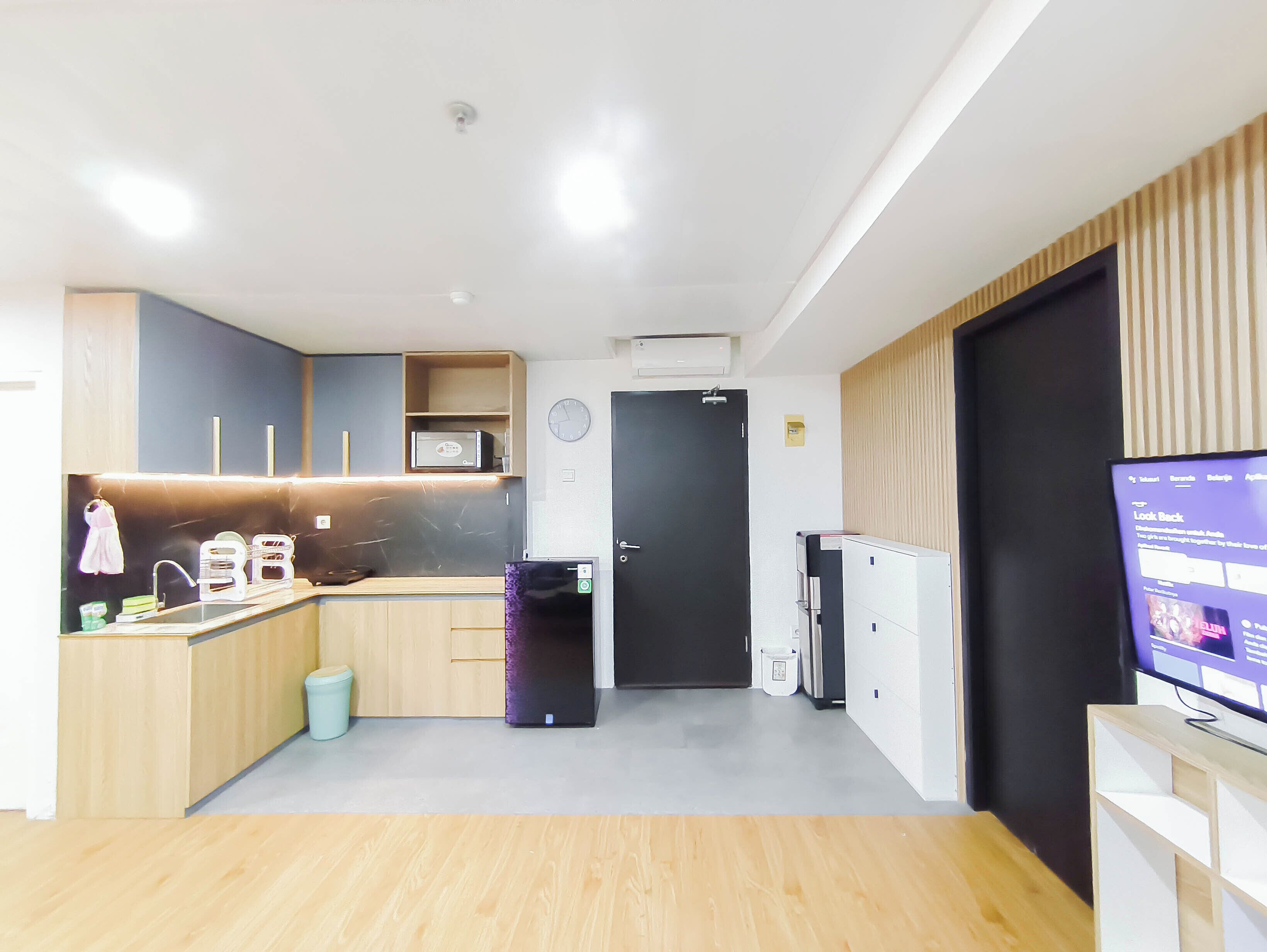 A compact kitchen with a microwave, sink, and cabinets, a black door, and a TV on a stand.