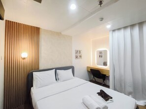 A hotel room with a bed, a desk, a chair, a mirror, and a curtain. - Cozy 2Br Apartment Grand Asia Afrika (Bandung)