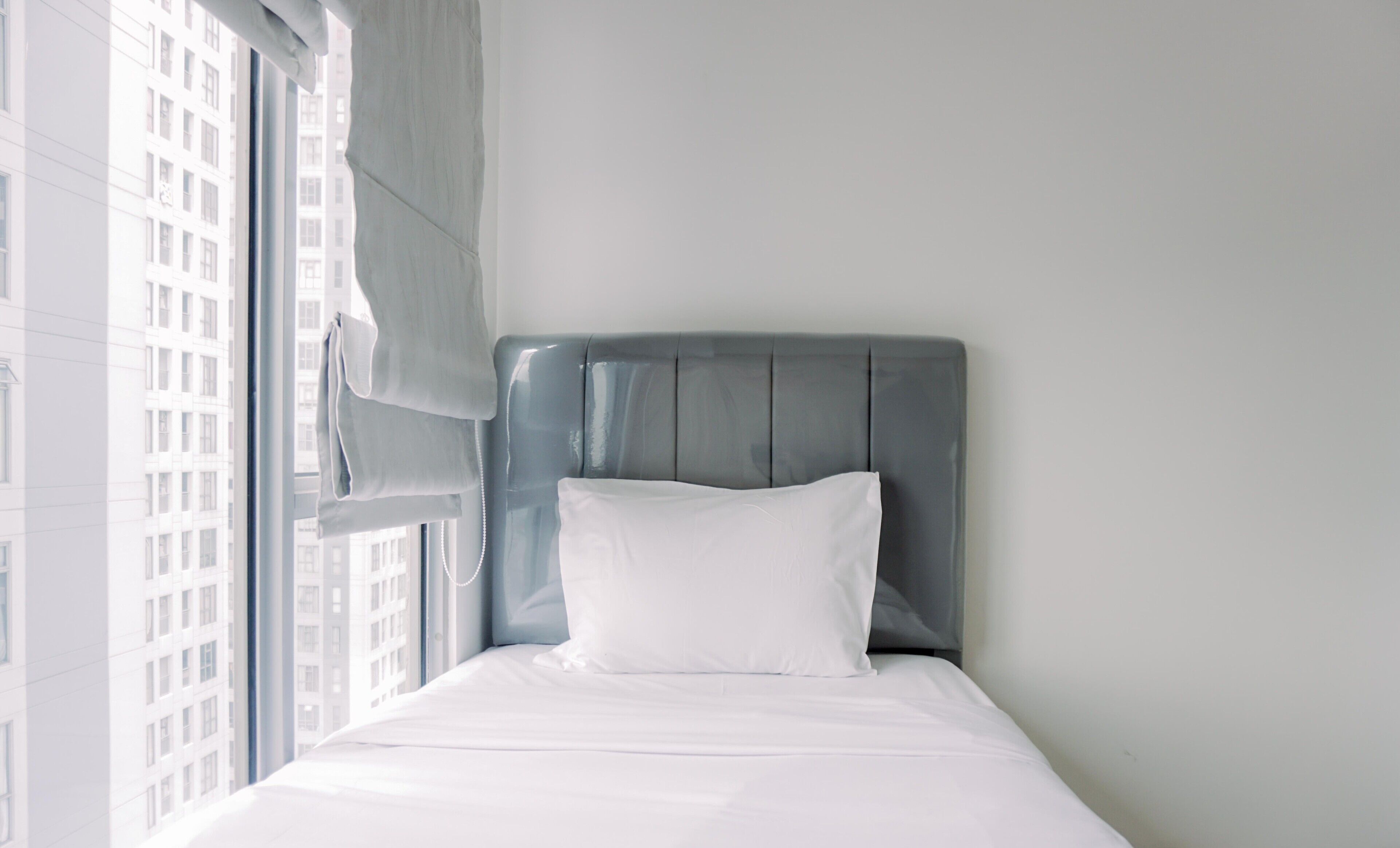 A hotel room with a bed, a window with curtains, and a view of a building outside.
