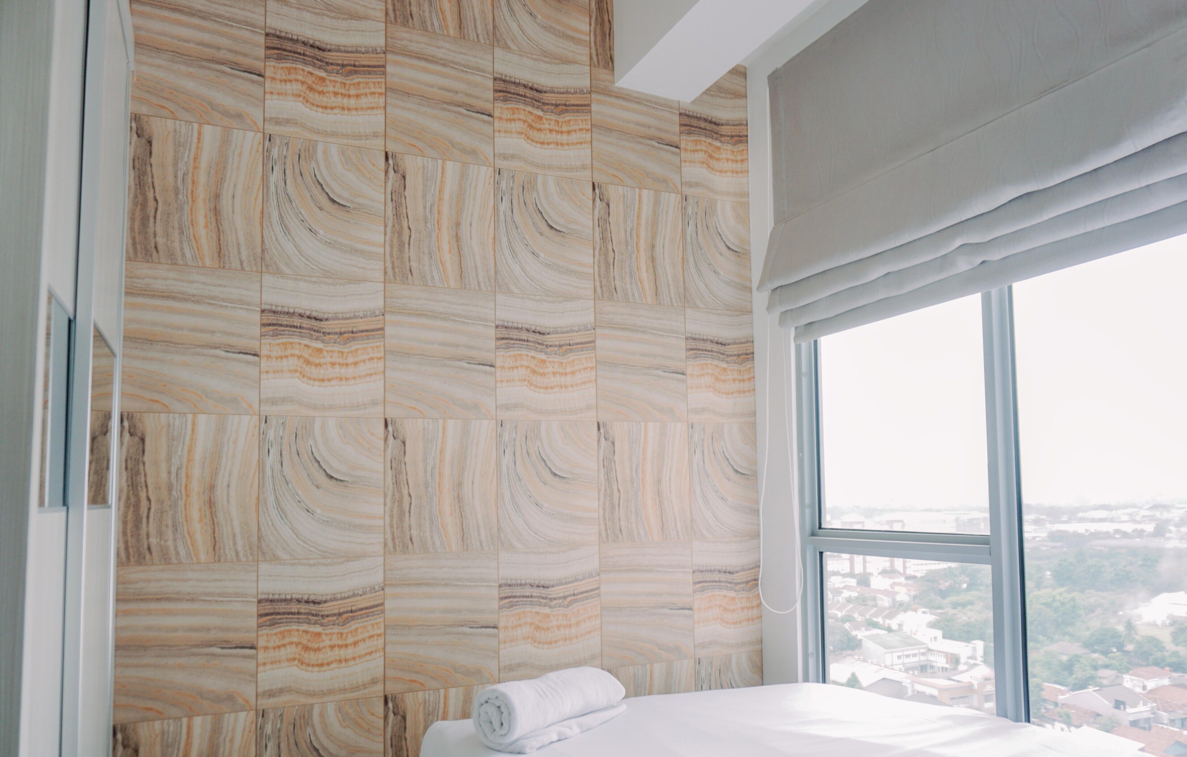 Un dormitorio con un ventanal grande, una cama y una pared con un diseño tipo mármol.