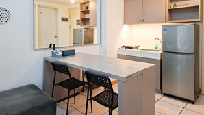 A compact kitchen with a refrigerator, a sink, and a dining area with chairs. - Simple 2Br Space At Apartment M-Town Residence (Gading Serpong)