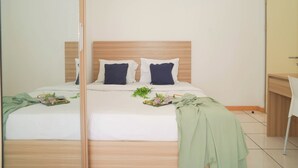 Un dormitorio con cabecera de madera, cama con ropa de cama blanca, dos almohadas, una mesita de noche y un espejo.