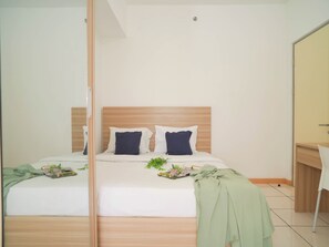 A bedroom with a wooden headboard, a bed with white bedding, two pillows, a bedside table, and a mirror. - 3 Pax Cheerful 2Br At M-Town Residence (Gading Serpong)