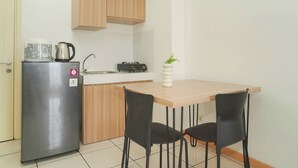 Una cocina compacta con refrigerador, tetera, lavamanos y una pequeña mesa con dos sillas.