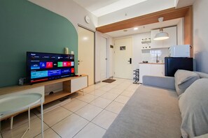 Quarto de hotel moderno com televisão de tela plana, sofá, mesa pequena e área de cozinha compacta.