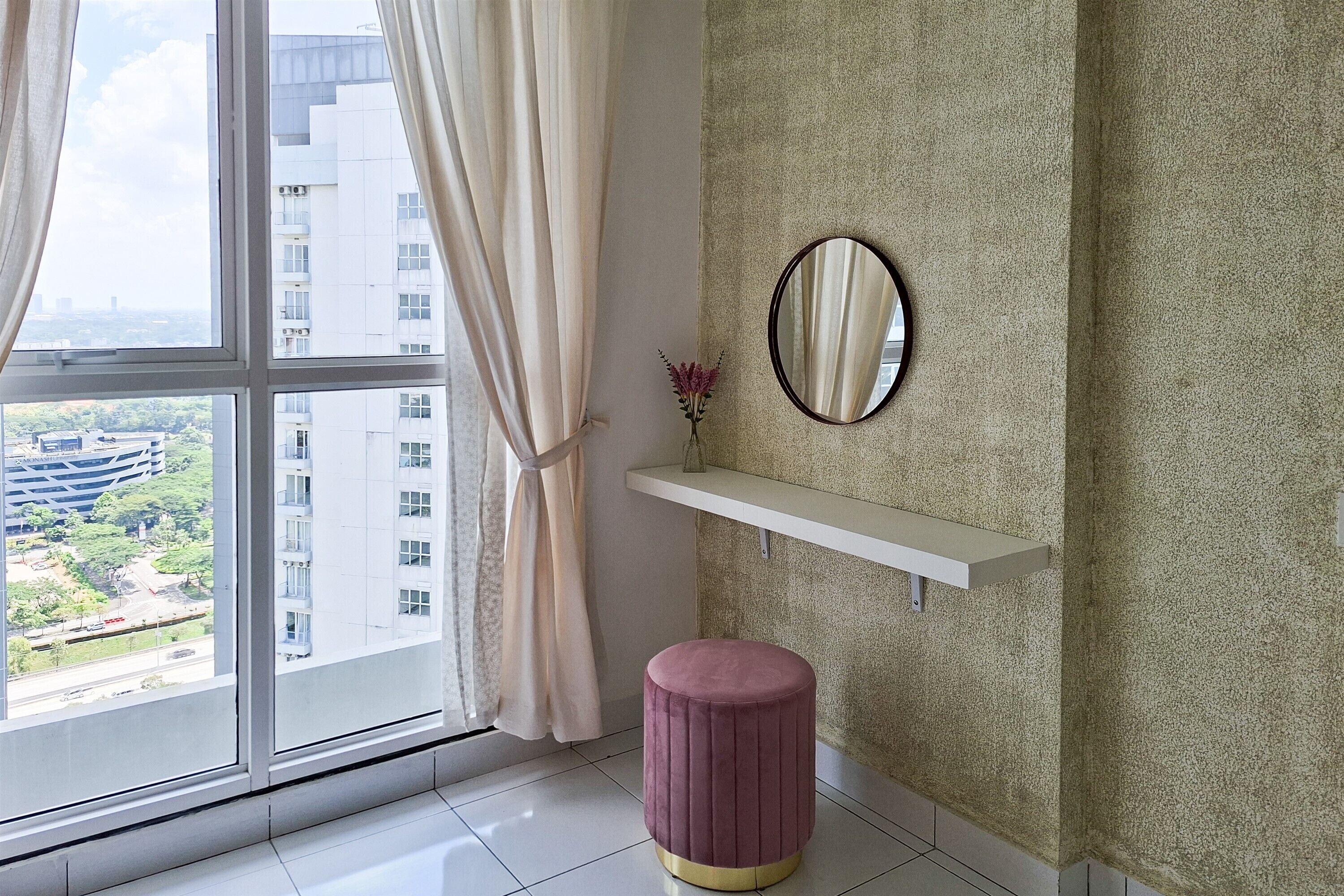 A room with a large window, a round stool, a mirror, and a shelf.