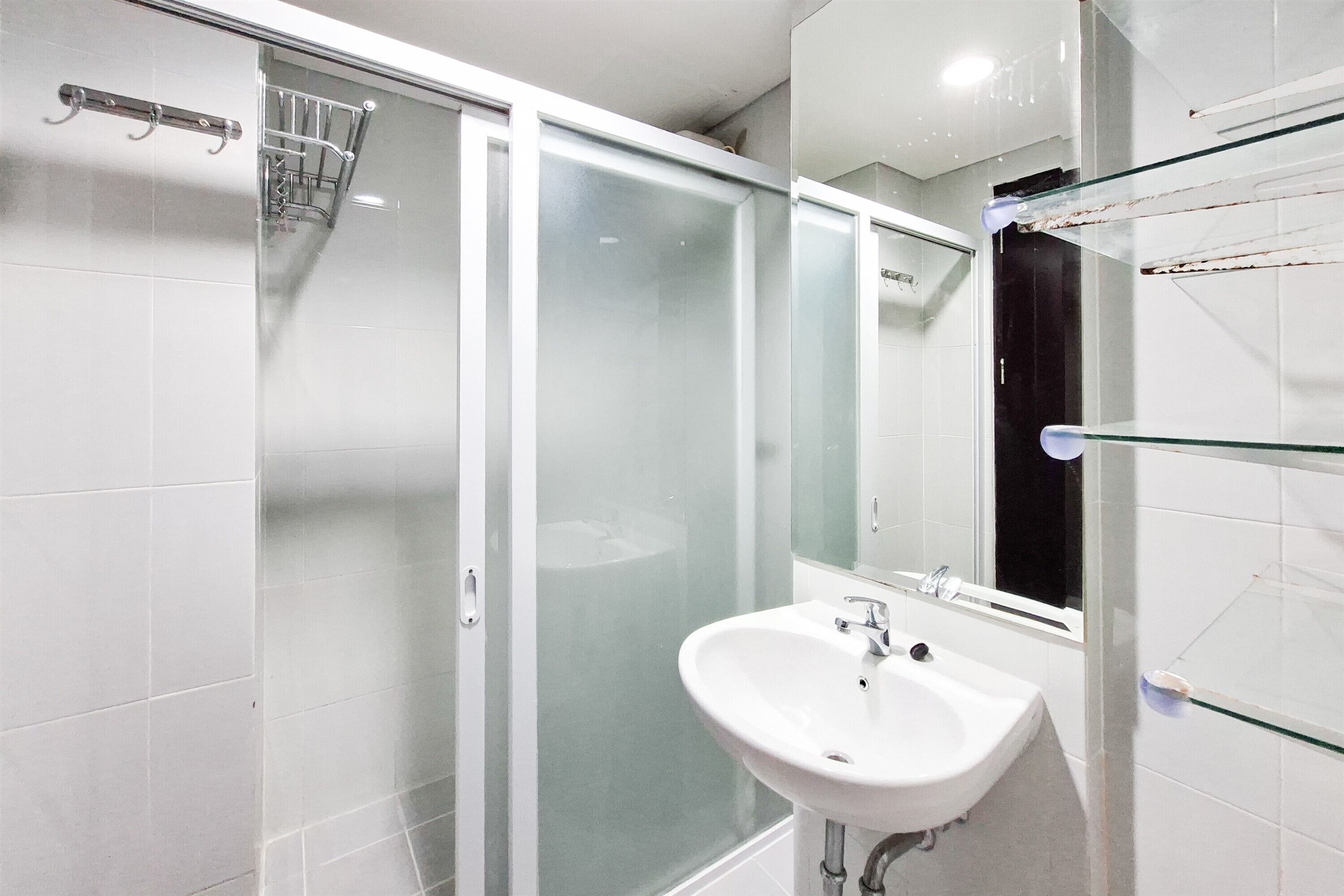 A modern bathroom with a glass-enclosed shower, a white sink, and a glass shelf.