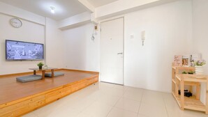 Ein Zimmer mit einer hölzernen Bank, einem Fernseher, einer Tür und einem kleinen Regal mit Büchern und einer Vase.