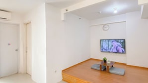 Ein Zimmer mit Holzboden, einem an der Wand montierten Fernseher, einem kleinen Tisch mit Kissen und einer Tür mit einem Schild.