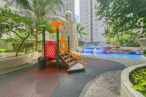 A playground with a slide and climbing structures, a small pool, and surrounding greenery. - Strategic And Homey 2Br At Bassura City Apartment (Jakarta)