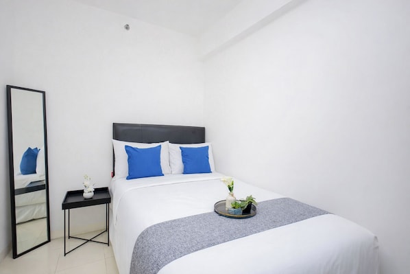 A neatly arranged hotel room with a bed, a bedside table, a mirror, and a small plant. - Strategic And Homey 2Br At Bassura City Apartment (Jakarta)