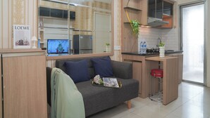 A modern kitchen with a built-in stove, a small dining area, and a sofa with cushions. - Warm 2Br For 3 Pax At Bassura City Apartment Near Shopping Center (Jakarta)
