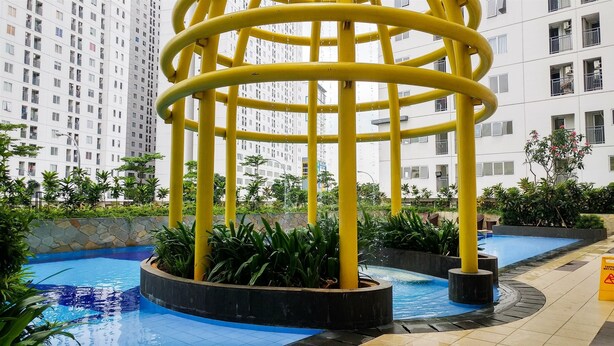 A modern building with a yellow spiral water feature in the courtyard. - Warm 2Br For 3 Pax At Bassura City Apartment Near Shopping Center (Jakarta)