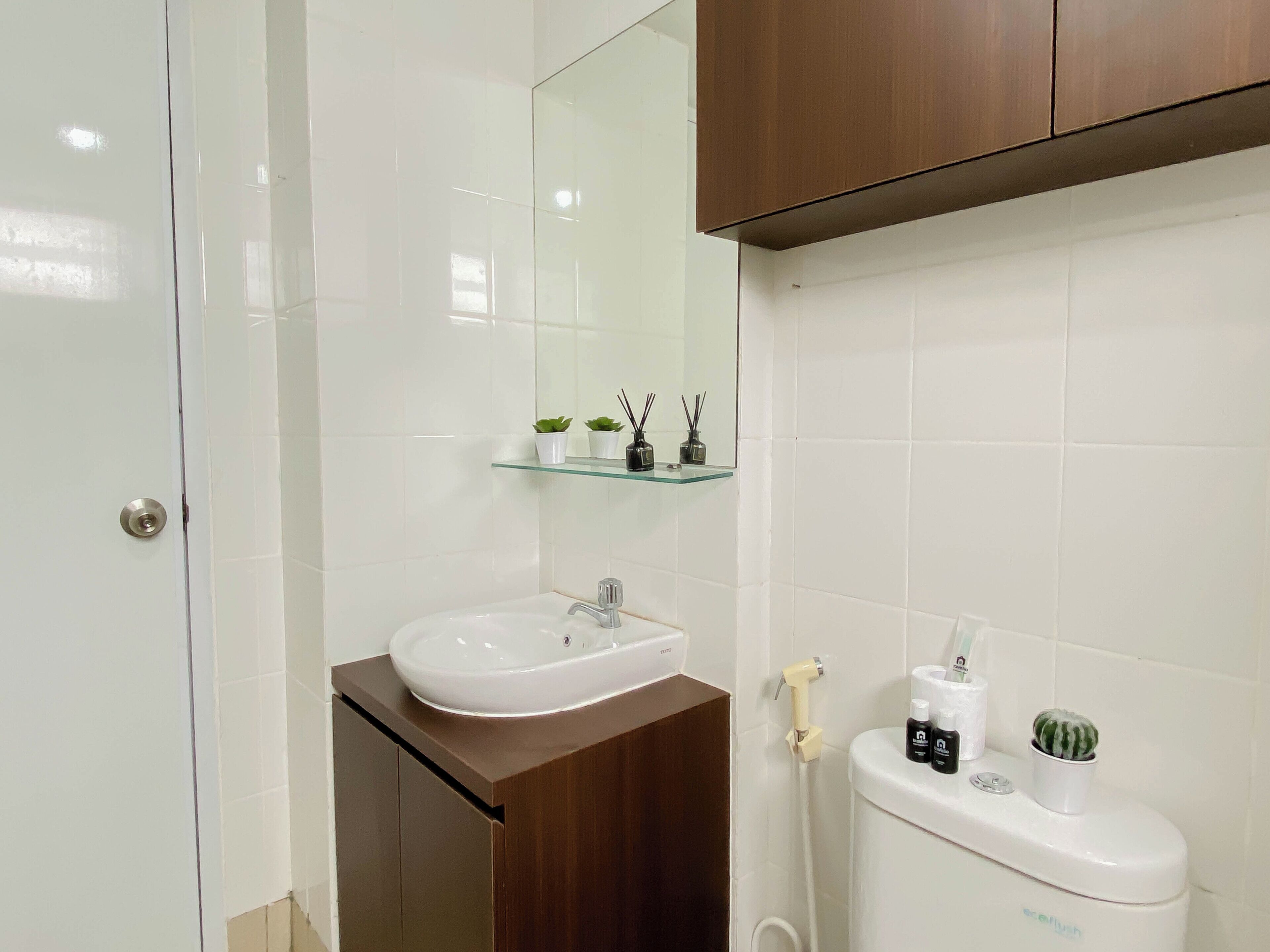 A bathroom with a white sink, a mirror, a glass shelf with toiletries, and a toilet.