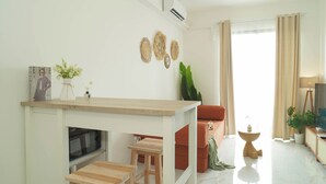 A modern living room with a kitchen area, a sofa, a coffee table, and a TV. - Homey 2Br For 3 Pax At Sky House Bsd Apartment (Pagedangan)