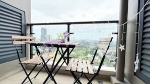 A balcony with a wooden table and chairs, a potted orchid, and a cityscape view. - Homey 2Br For 3 Pax At Sky House Bsd Apartment (Pagedangan)