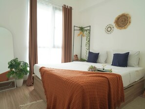 A bedroom with a bed, a bedside plant, a mirror, and a wall decoration. - Homey 2Br For 3 Pax At Sky House Bsd Apartment (Pagedangan)