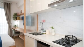 A compact kitchen with a gas stove, a sink, and a dishwasher. There is a small dining area with a chair and a table. - Studio Japandi Areum Residence At Sky House Bsd (Pagedangan)