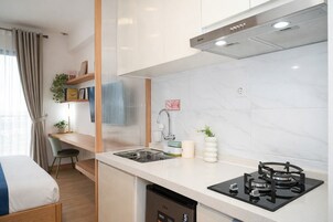 Uma cozinha compacta com fogão a gás, pia e lava-louças. Há um pequeno espaço de refeições com uma cadeira e uma mesa.